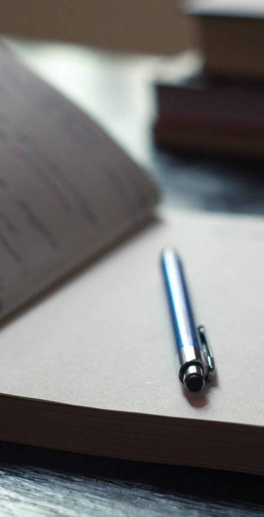 Open Notepad with handwritten notes with blue pen, books in the background